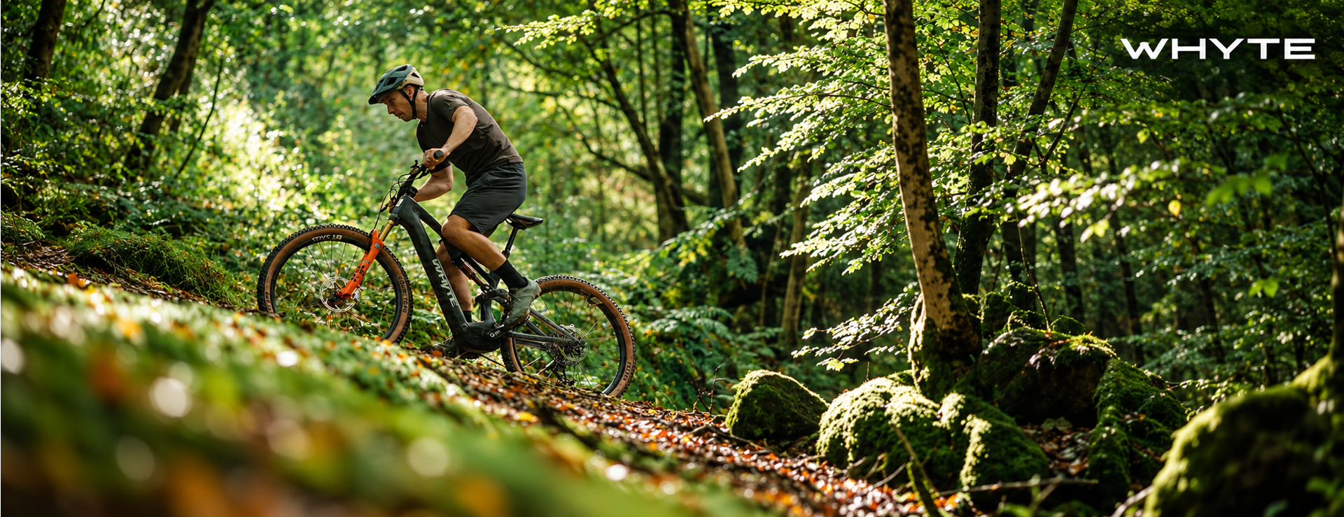 Cyclist riding a Whyte E-Lyte mountain bike along a sunlit woodland trail