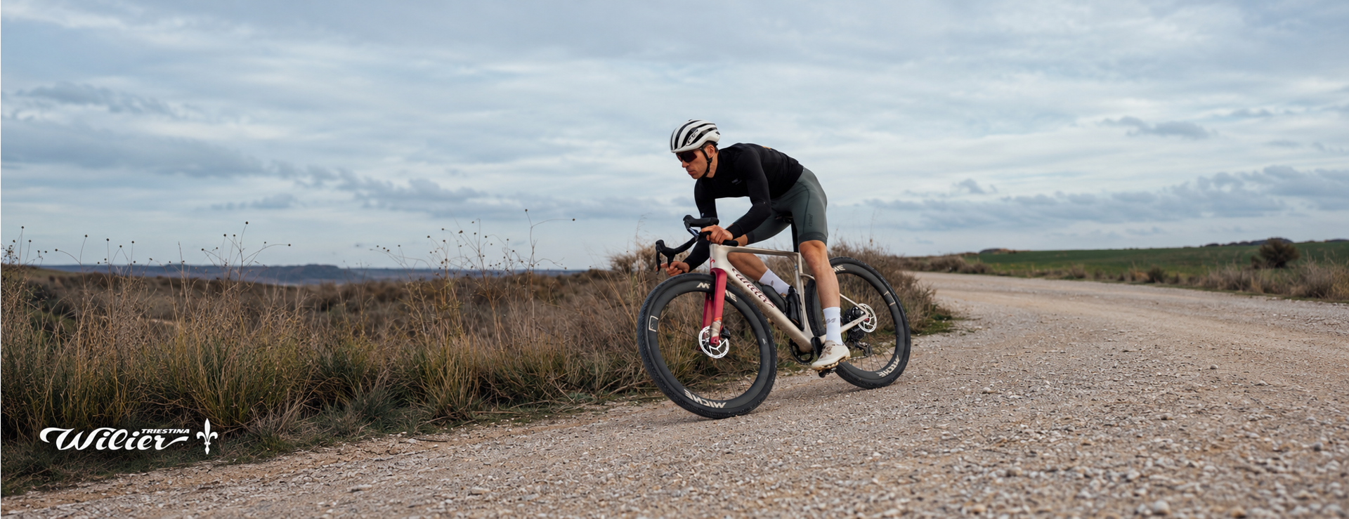 Cyclist riding a cream and red Wilier gravel bike along a winding gravel track